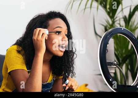 Young influencer woman making a makeup video blog for social media. It is recorded with a smartphone and with a light ring at home. Concept of beauty Stock Photo