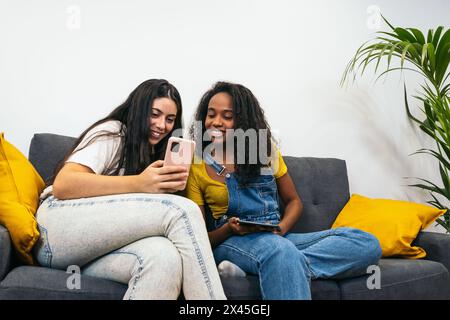 Connected at home: Two young women using mobile devices Stock Photo