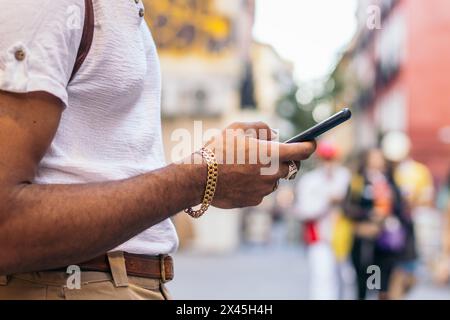 Unrecognizable black man using smartphone leaning on a wall in the city street Stock Photo