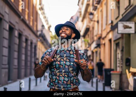 Stylish black man with alternative hipster look walking through the streets of a city on a sunny summer day. he smiles happily Stock Photo