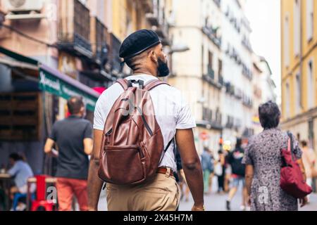 Rear view of a stylish black man with beret and leather backpack walking on a city street in summer Stock Photo