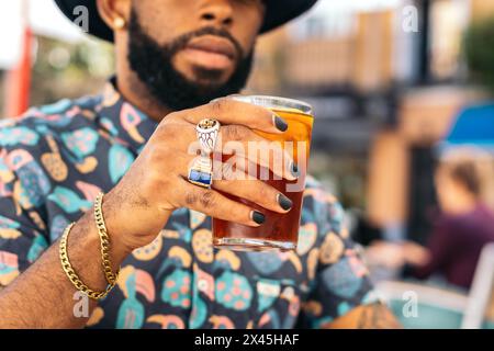 Stylish black man with painted nails and a hat having a drink sitting on a terrace in the city of Madrid on a summer day Stock Photo