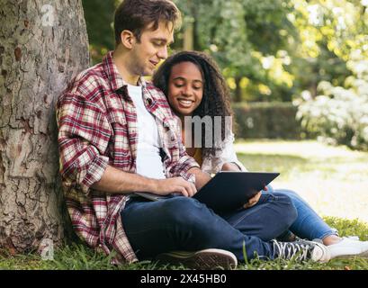 Young couple of multiracial students sitting in the park using a laptop. They work together and have fun Stock Photo