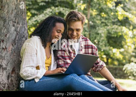 Young couple of multiracial students sitting in the park using a laptop. They work together and have fun Stock Photo