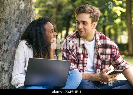 Young couple of multiracial students sitting in the park using a laptop. They work together and have fun Stock Photo