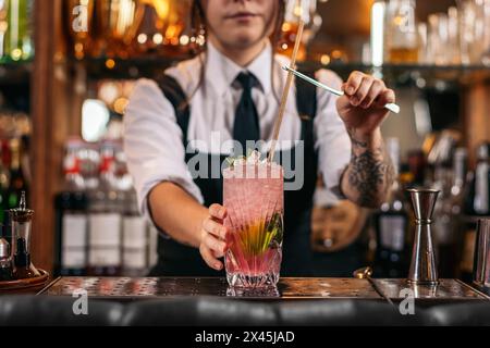 Close-up of a female bartender pouring a cocktail and decorating it with garnish Stock Photo