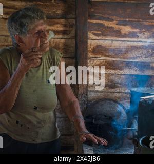 A coffee farmers wife smoking a cigar in the farmhouse while making the coffee, near Vinales, Cuba Stock Photo