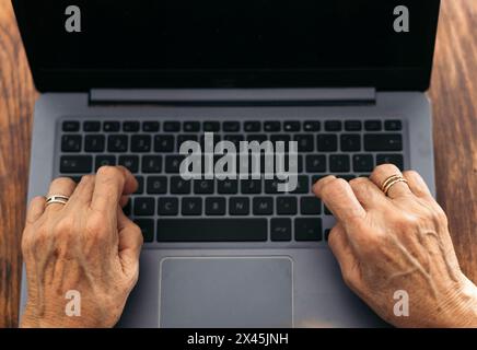 closeup of the hands of an unrecognizable old woman using the laptop while browsing the internet at home. Stock Photo