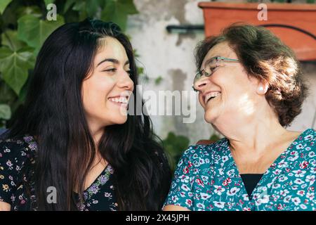 Grandmother and granddaughter talking and laughing together sitting in the backyard of the house Stock Photo