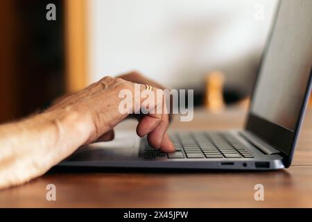 closeup of the hands of an unrecognizable old woman using the laptop while browsing the internet at home. Stock Photo
