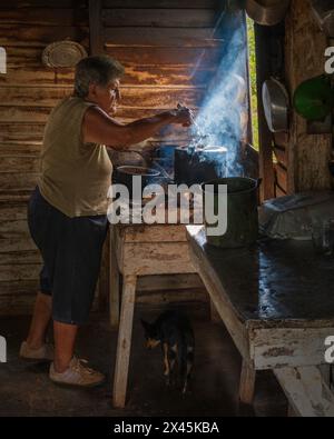 A coffee farmers wife smoking a cigar in the farmhouse while making the coffee, near Vinales, Cuba Stock Photo