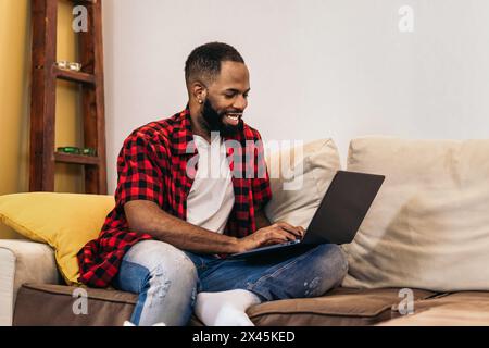 Smiling black man working remotely from home with laptop computer. Telecommuting and home office concept. Stock Photo