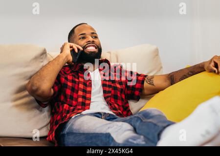 African american man lying on sofa making a call with smartphone relaxed at home Stock Photo