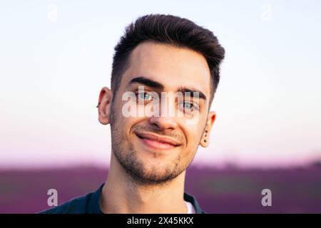Portrait of a young man with blue eyes looking at the camera with a genuine smile in a lavender field at sunset Stock Photo
