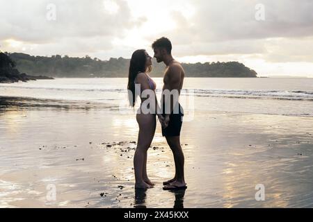 Couple standing on a beautiful beach at sunset in Costa Rica, looking at each other and about to kiss Stock Photo
