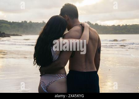 Romantic photo of a couple embracing on the beach watching sunset Stock Photo