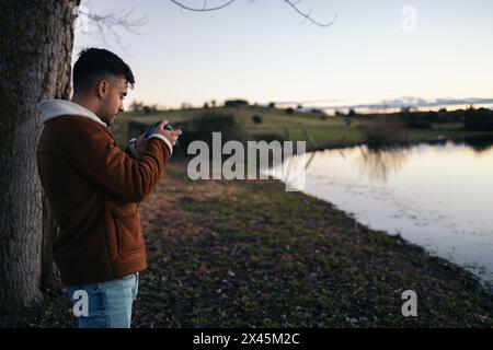Young photographer man making sunset photos of a nice lake in nature. He reviews the pictures he has taken on the camera screen Stock Photo