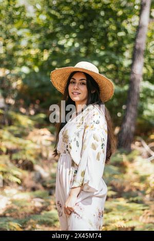 Beautiful brunette woman with a straw hat walking in the forest Stock Photo