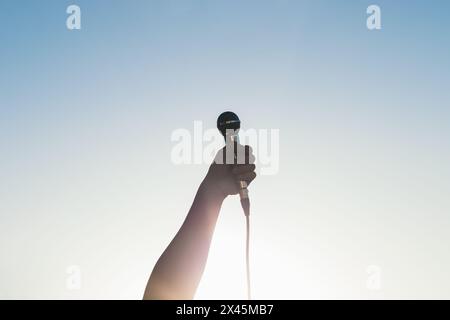 man hand holding a microphone outdoors with sunlight reflects Stock Photo