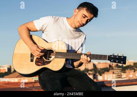 young man sitting playing acoustic guitar on a rooftop Stock Photo