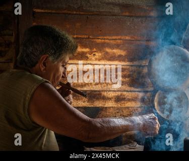 A coffee farmers wife smoking a cigar in the farmhouse while making the coffee, near Vinales, Cuba Stock Photo