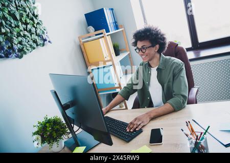 Photo of cool smart employee wear khaki shirt eyeglasses communicating instagram twitter telegram facebook indoors workstation workplace Stock Photo