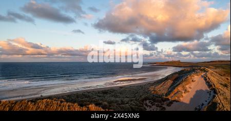 Aerial panorama landscape view of sand dunes and sandy beach at  Embleton Bay and Dunstanburgh Castle on the England Coast Path at sunset Stock Photo