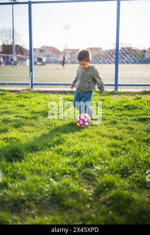 Captured in mid-play, this toddler boy focuses on the soccer ball, illustrating a 3-year-old's engagement with football on grass. A vibrant scene capt Stock Photo