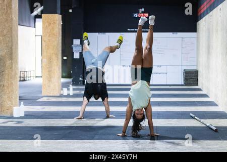 Full body of strong Hispanic sportsman and sportswoman doing handstand exercise for practicing balance during fitness training in gym Stock Photo