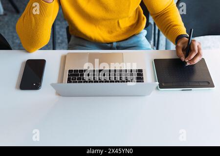 Cropped unrecognizable African American male entrepreneur working on graphic tablet using stylus and on netbook in office Stock Photo