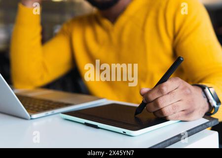 Cropped unrecognizable African American male entrepreneur working on graphic tablet using stylus and on netbook in office Stock Photo