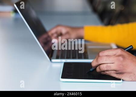 Cropped unrecognizable African American male entrepreneur working on graphic tablet using stylus and on netbook in office Stock Photo