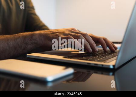 Crop anonymous male worker browsing modern portable netbook while sitting at table with smartphone in light room during work process Stock Photo