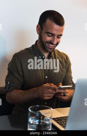 Smiling male worker text messaging on cellphone while sitting at table with netbook Stock Photo