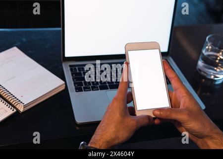 From above of crop unrecognizable male worker text messaging on cellphone with empty screen while sitting at table with netbook Stock Photo