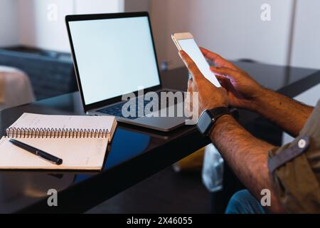 Crop unrecognizable male worker text messaging on cellphone with empty screen while sitting at table with netbook Stock Photo