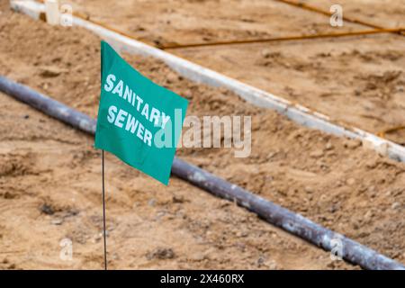 Small green flag with white lettering, warning of an underground sanitary sewer line, at a new home construction site. Stock Photo