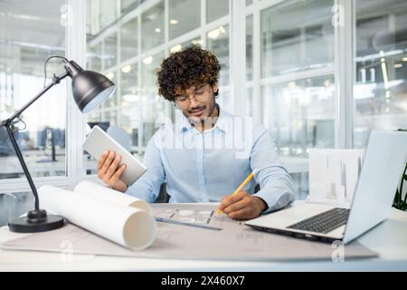 A focused male architect examining architectural models and blueprints in a modern office. He is analyzing designs and planning with concentration. Stock Photo