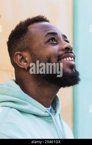 Happy adult African American hipster male laughing while standing against yellow wall on street Stock Photo