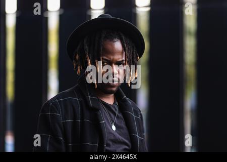 Informal bearded ethnic man with dreadlocks and in hat looking away standing on street Stock Photo