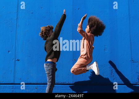 Side view of excited African American curly haired boy and girl having fun and giving high five to each other while enjoying sunny day together on str Stock Photo