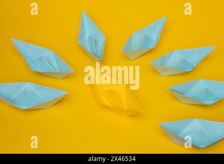 A group of blue paper boats surrounded one yellow boat, the concept of bullying, search for compromise. Stock Photo