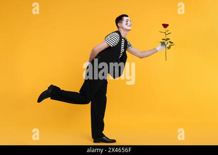 Funny mime artist with red rose posing on orange background Stock Photo