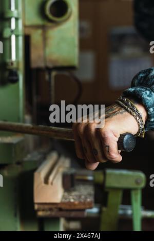 Crop unrecognizable tattooed male carpenter drilling wooden board using lathe during work in joinery Stock Photo