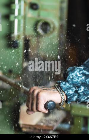 Crop unrecognizable male tattooed carpenter holding handle of woodworking machine while working in professional joinery Stock Photo