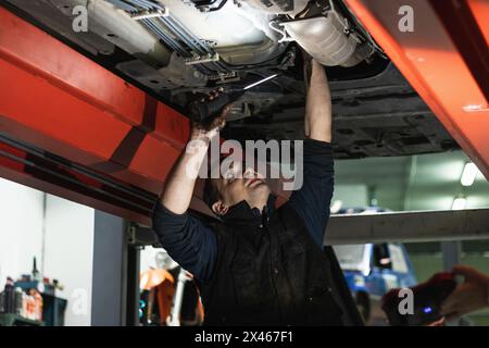 From below of concentrated adult male mechanic in uniform repairing car silencer while working in auto service Stock Photo