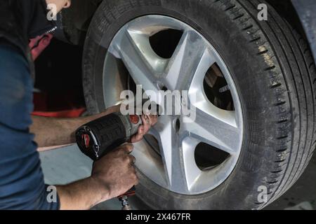 Crop anonymous male mechanic using automatic screwdriver while changing wheels during car maintenance in garage Stock Photo