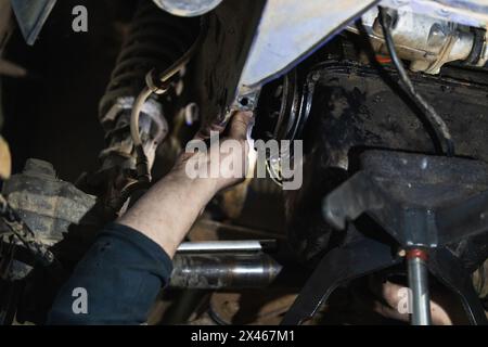 From below of anonymous adult male mechanic in uniform repairing car silencer while working in auto service Stock Photo