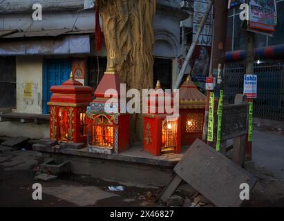 Four small shrines with lighting next to a large tree trunk on the side of a road in Varanasi, India. Stock Photo