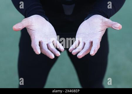 Crop anonymous athlete in black sportswear demonstrating hands covered with white powder chalk while preparing for exercise Stock Photo